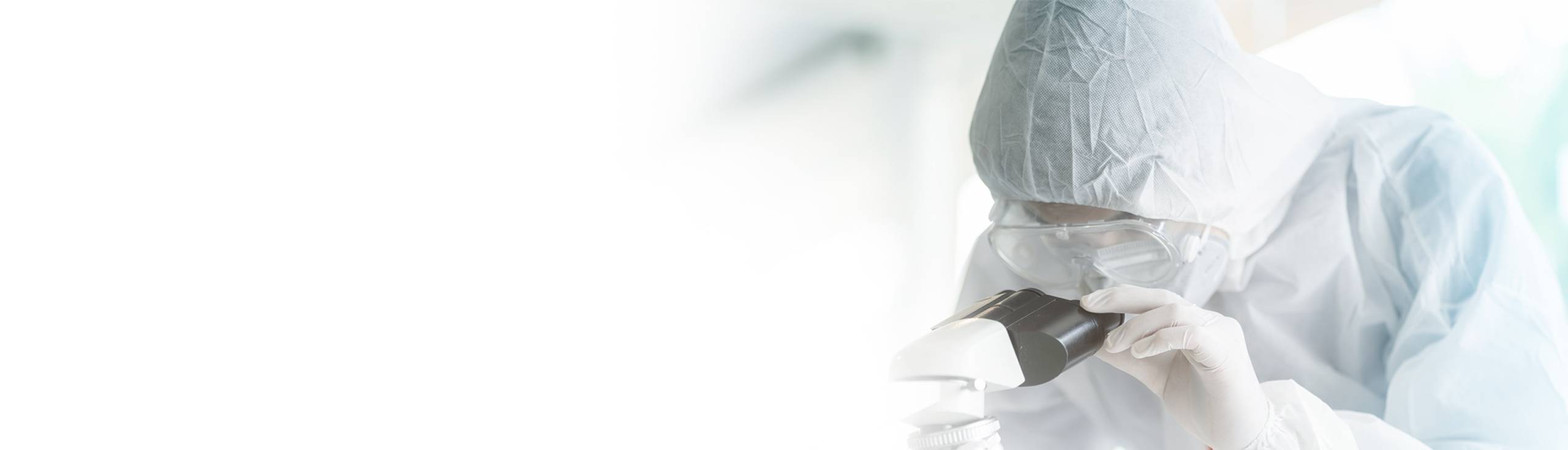 scientist in clean room outfit looking into a microscope
